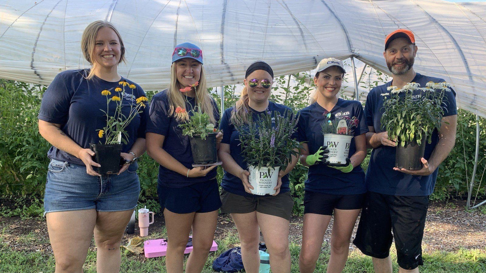 OMB Marketing team smiling in front of a greenhouse preparing to plant flowers for a 2023 United Way Day of Caring planting and beautification event.