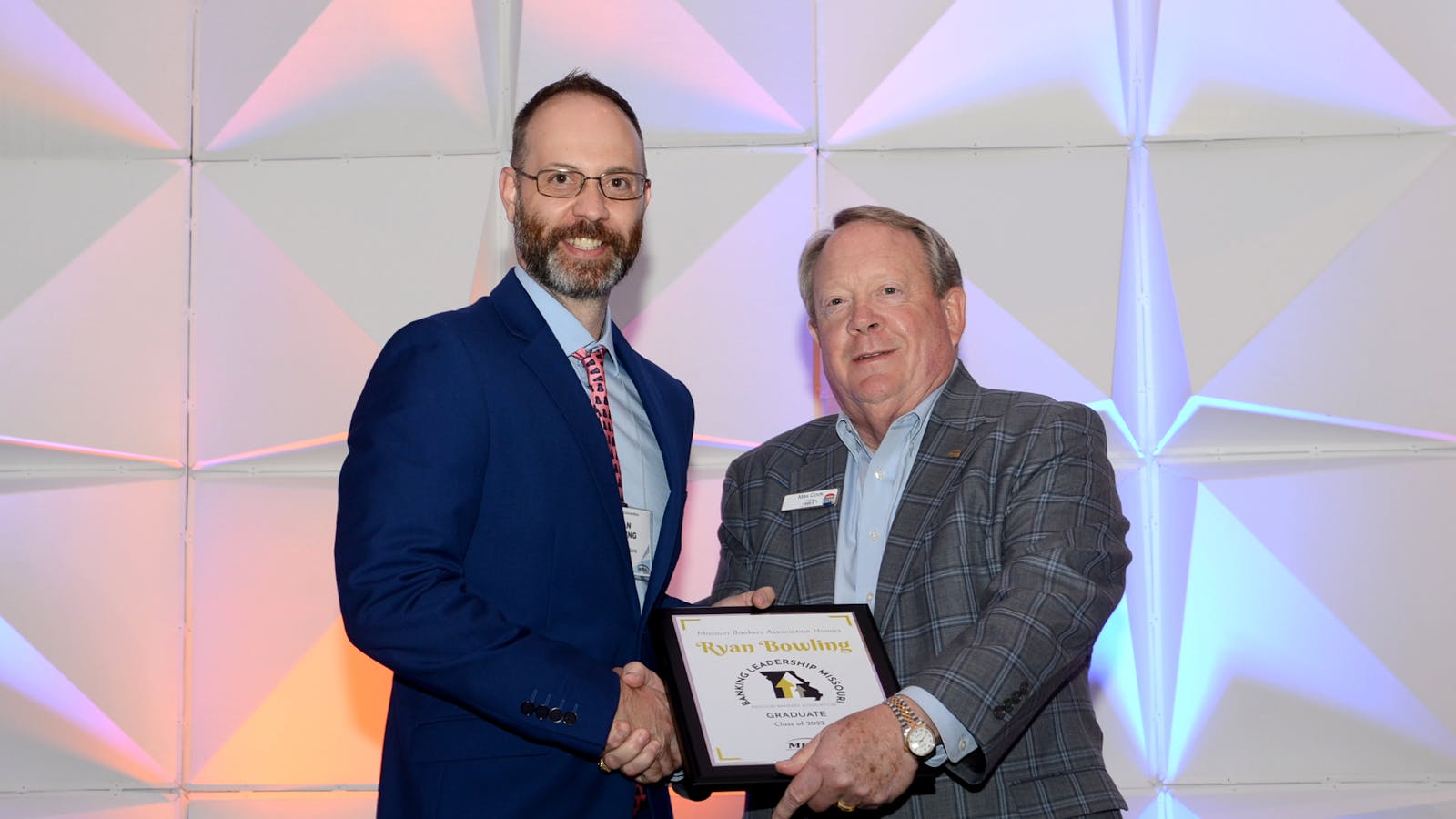 Ryan Bowling shaking hands with MBA President Max Cook in front of a photo backdrop.