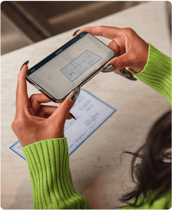 Woman with green sweater is using OMB mobile banking app to deposit a check
