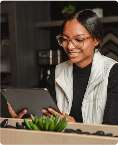 a young african american woman is sitting in a kitchen wearing a black shirt with a white best and looking at her iPad