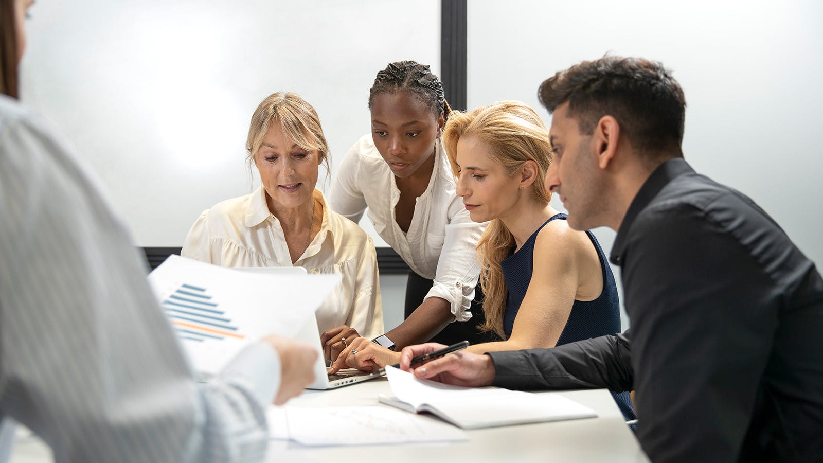 Four diverse business-people sitting closely at a table talking and examining charts