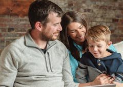 a dad and mom are sitting on a couch with their small son sitting on their lap while they look at a computer