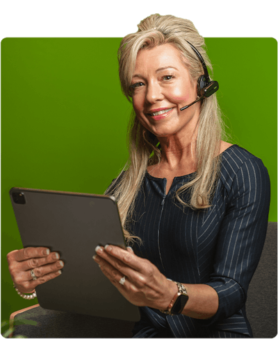 Woman with a black dress and blonde hair is sitting down holding an iPad and is wearing a headset