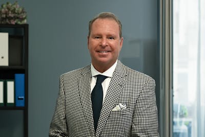 Cramer Hass sitting in an office wearing a black and white checkered sports coat and smiling