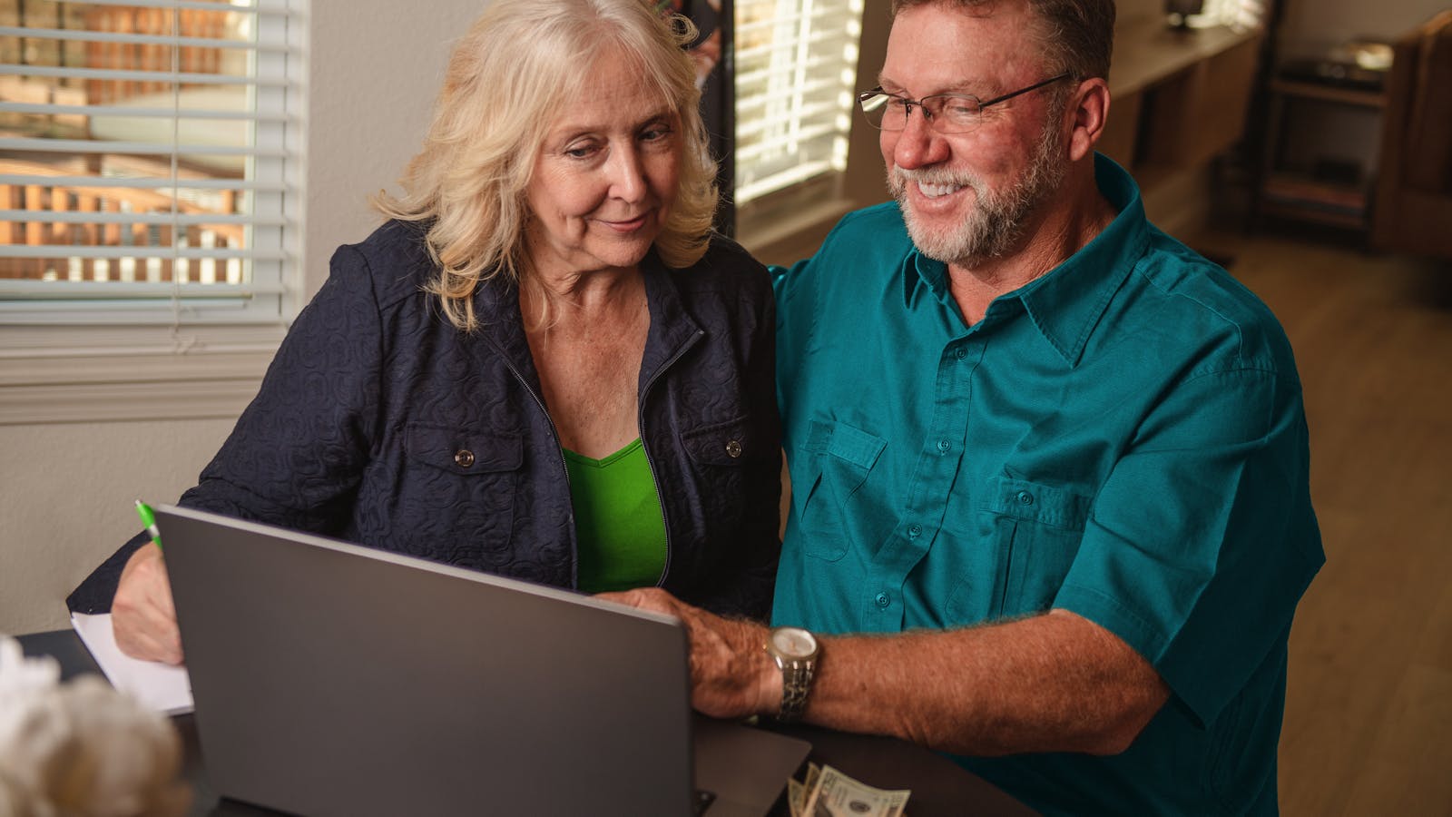 An elderly Caucasian couple smiling at their laptop.