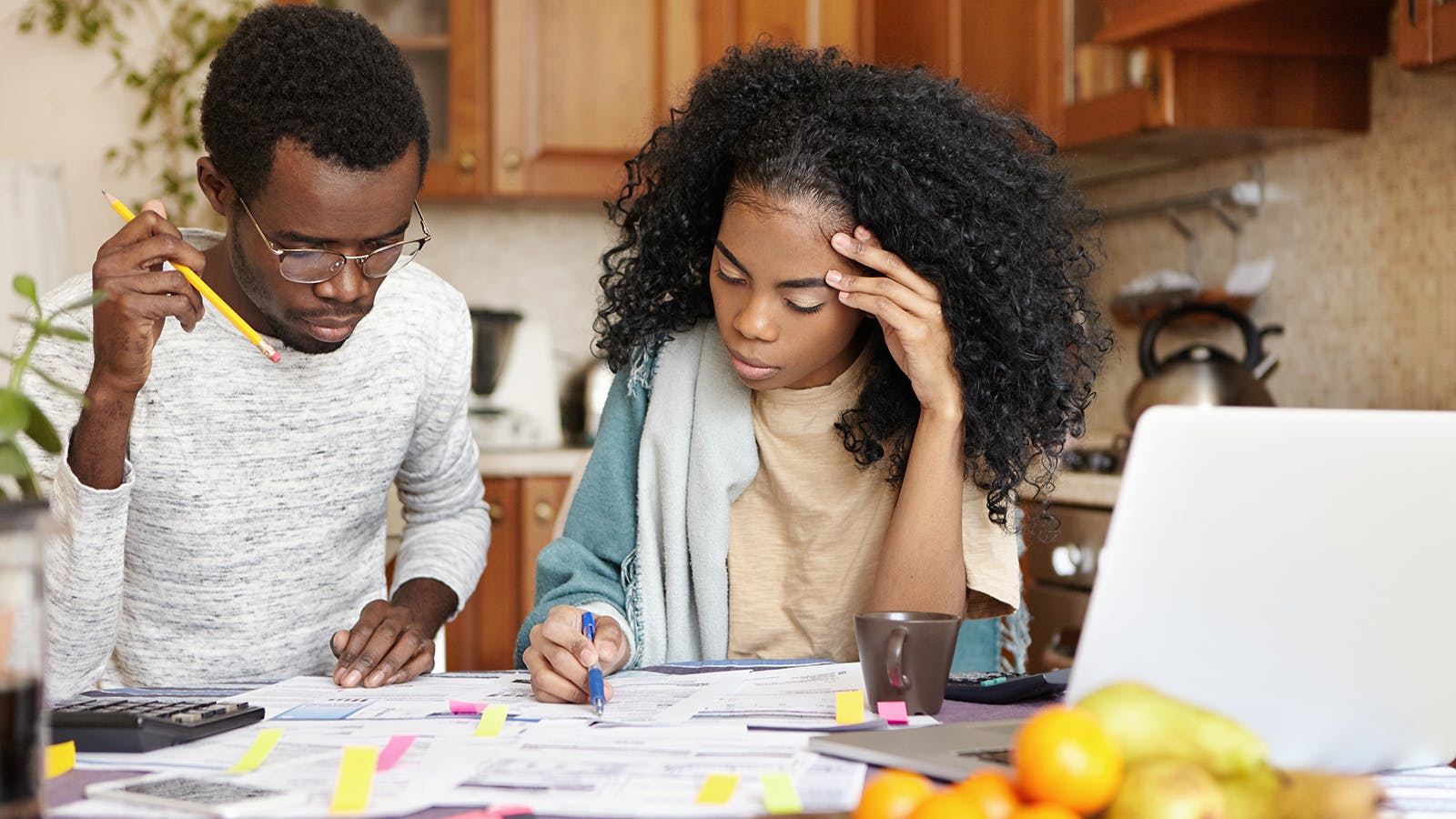 A young couple looking concerned over budget and loan paperwork with cups of coffee and a laptop nearby