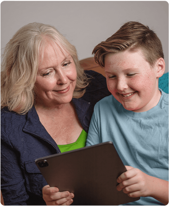 Grandma is sitting with her grandson and they are looking at an iPad