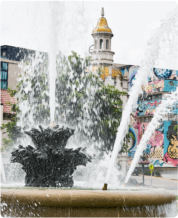 A fountain in Kansas City with a brightly colored mural on the wall behind it