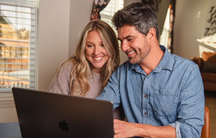 a couple is sitting down at a table looking at something on their computer and smiling