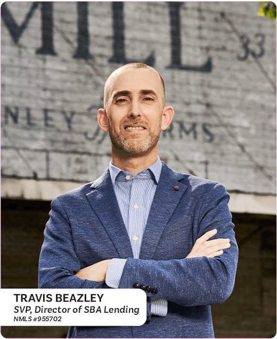 Travis Beazley Director of SBA lending standing in front of a mill with his arms crossed while smiling