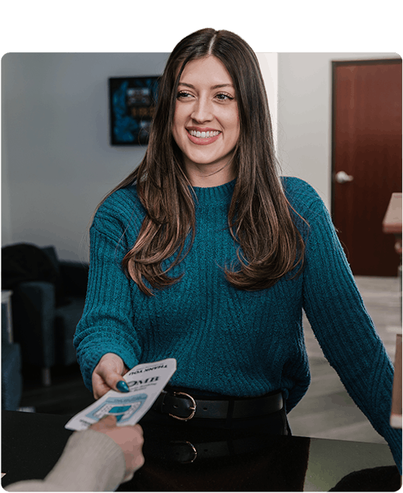a customer wearing a teal blue sweater is standing at a teller window receiving a cash envelope