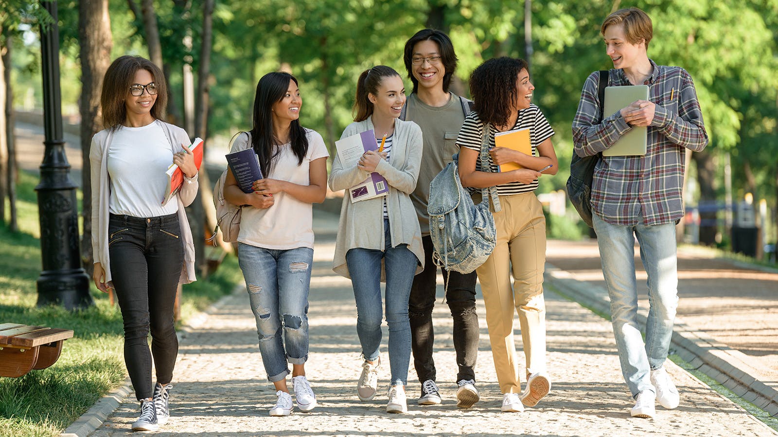 Six smiling college students holding textbooks while walking together on a sidewalk