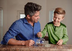 Father and son counting money as they put it into a piggy bank