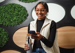Young woman smiling at phone in black shirt and white vest with glasses