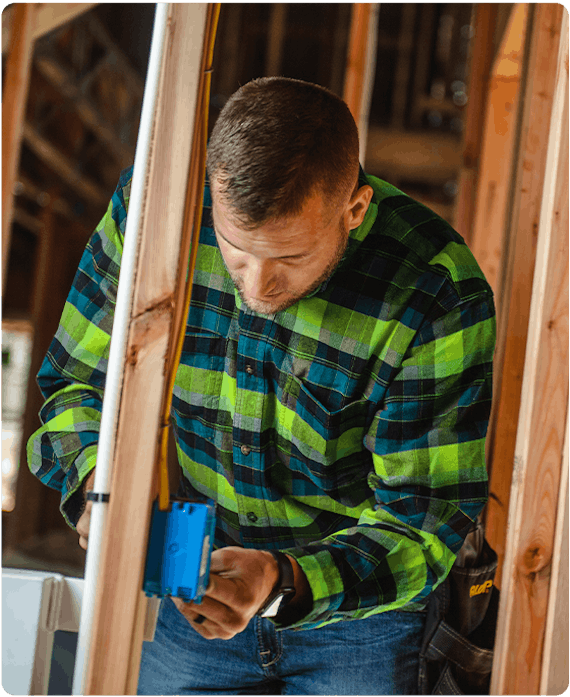 man wearing green and blue flannel button up shirt is installing an outlet in construction area