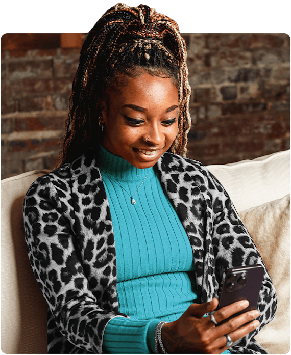 A woman with leopard cardigan and blue sweater is sitting down and looking at her phone